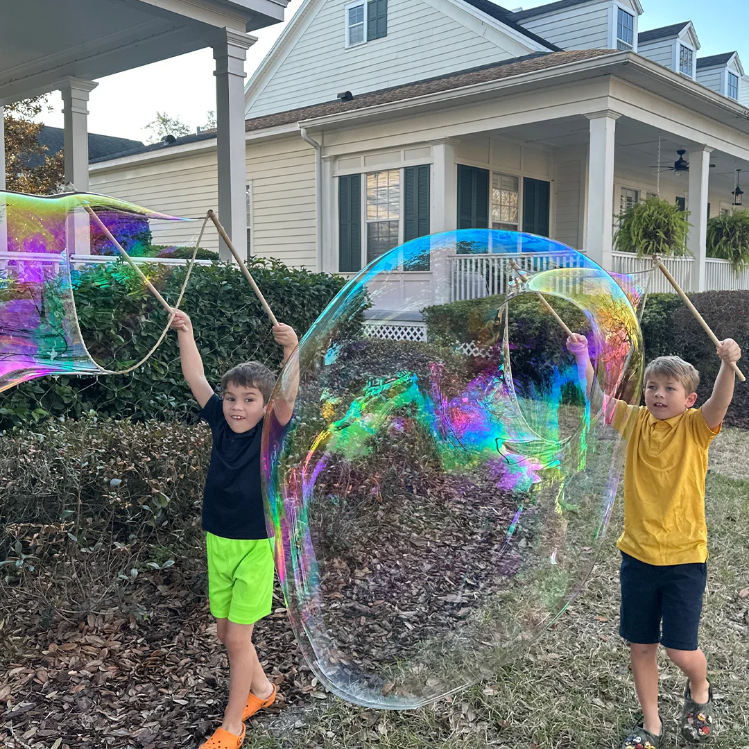 Two children holding separate BubbleStix wooden wand sets outdoors