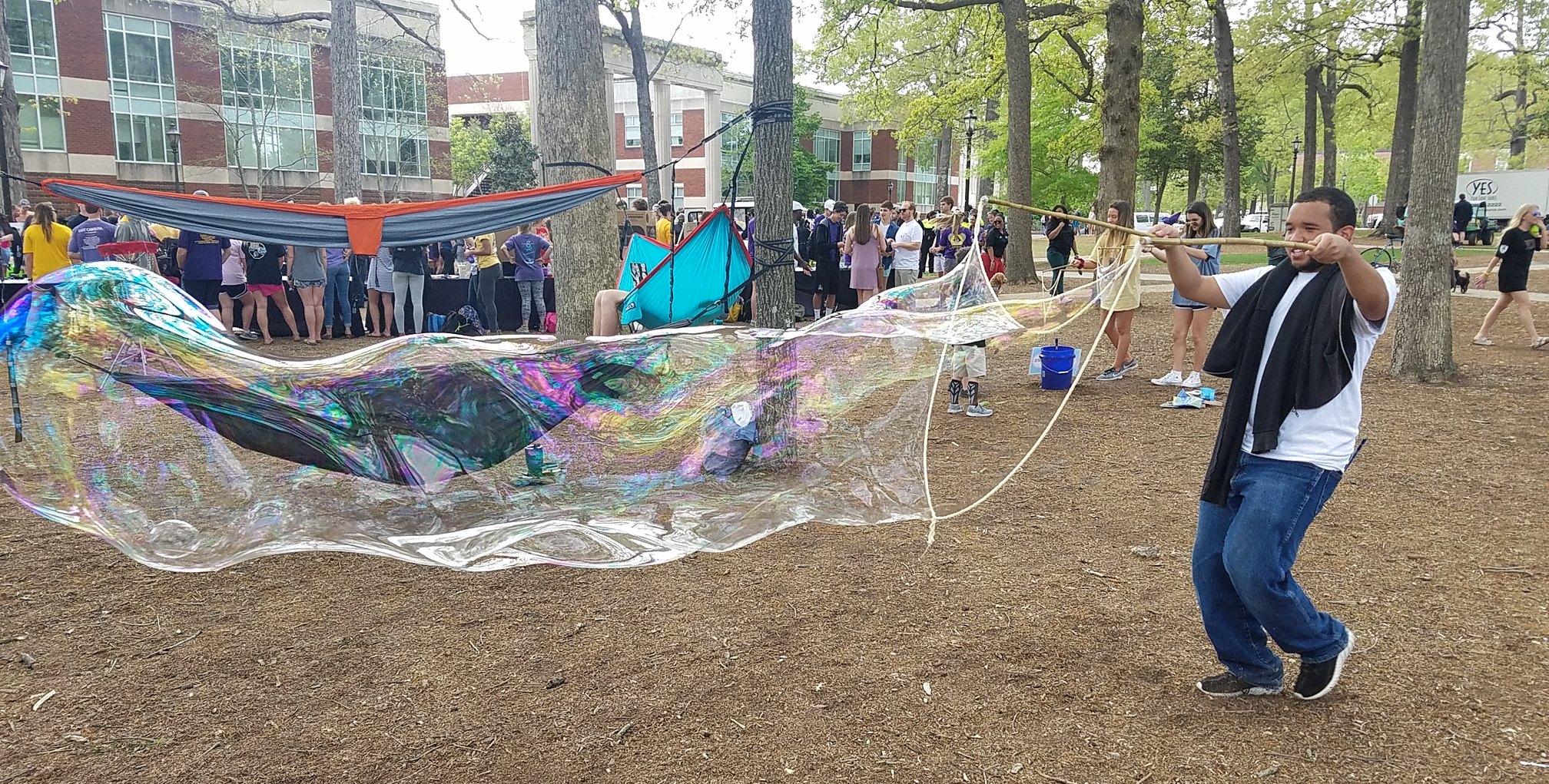 BubbleStix participant holding a complete wooden wand set open beneath a giant rainbow bubble at an outdoor festival