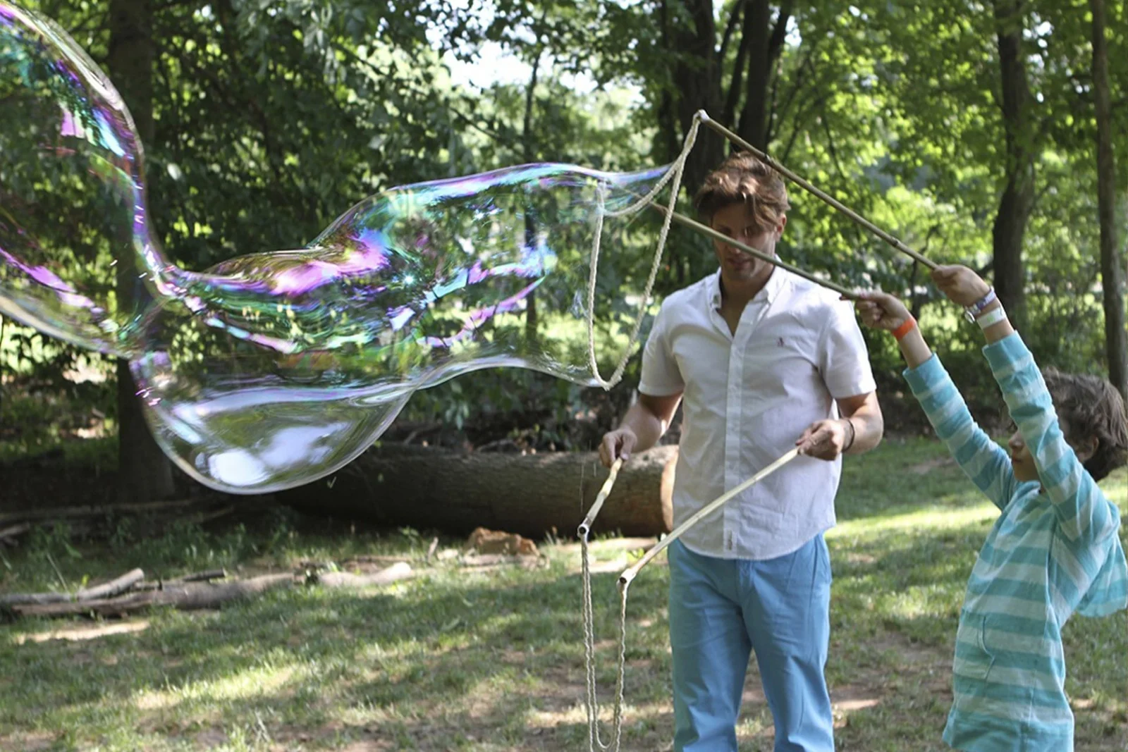 Adult and child using separate BubbleStix wand sets in a wooded outdoor space
